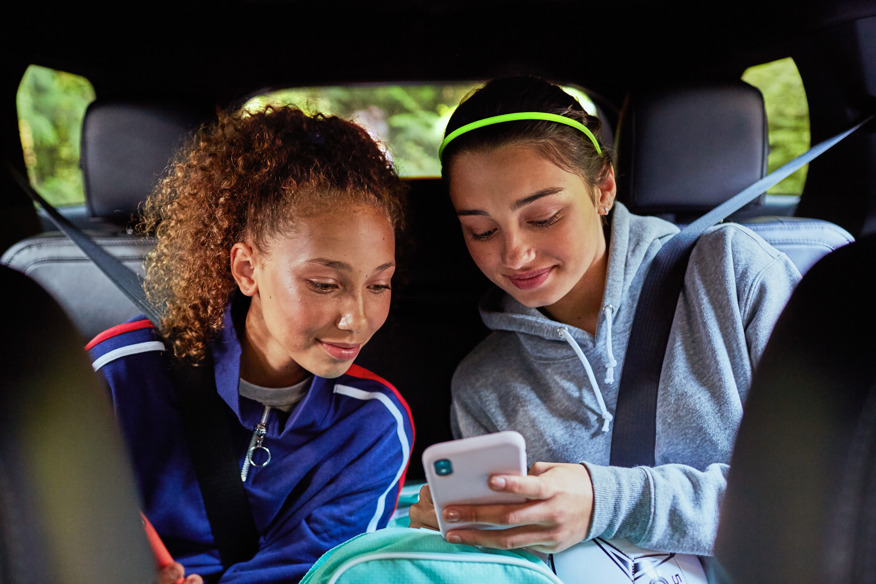 Teenage girls watch a video on a phone in the car. Lifestyle image by Leah Verwey