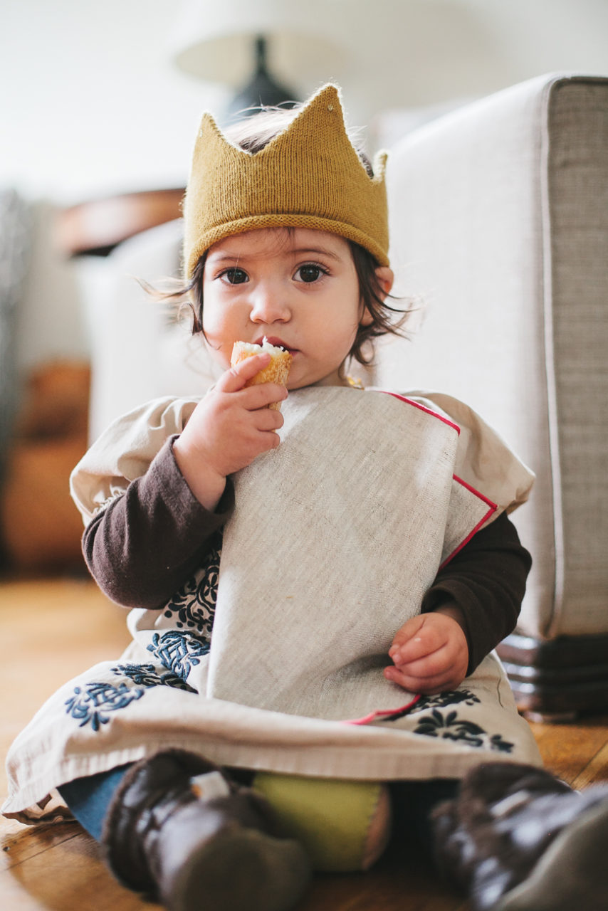 A toddler in a crown eats some bread. 