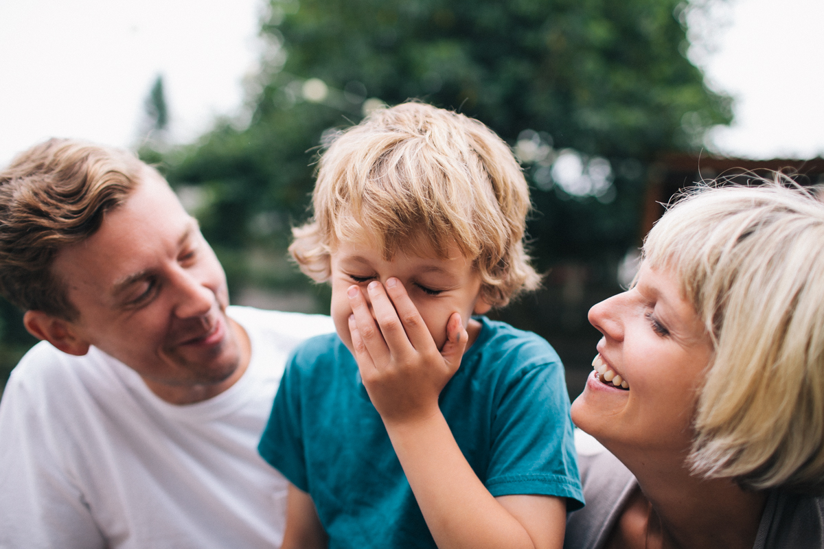 A young kid laugh with his parents in a lifestyle image by Leah Verwey